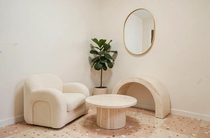 Petit espace de vie avec mobilier aux formes arrondies : fauteuil bouclé, table basse circulaire en travertin et miroir ovale