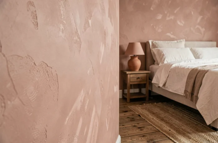 Mur en peinture à la chaux rose poudré avec variations organiques naturelles dans une chambre aux tons chauds et artisanaux