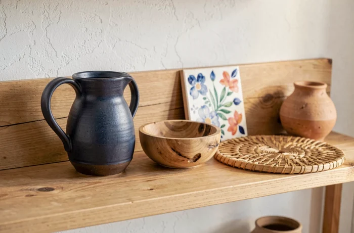 Objets artisanaux et locaux disposés en vignette : pichet en grès émaillé, bol sculpté en bois et céramique peinte à la main